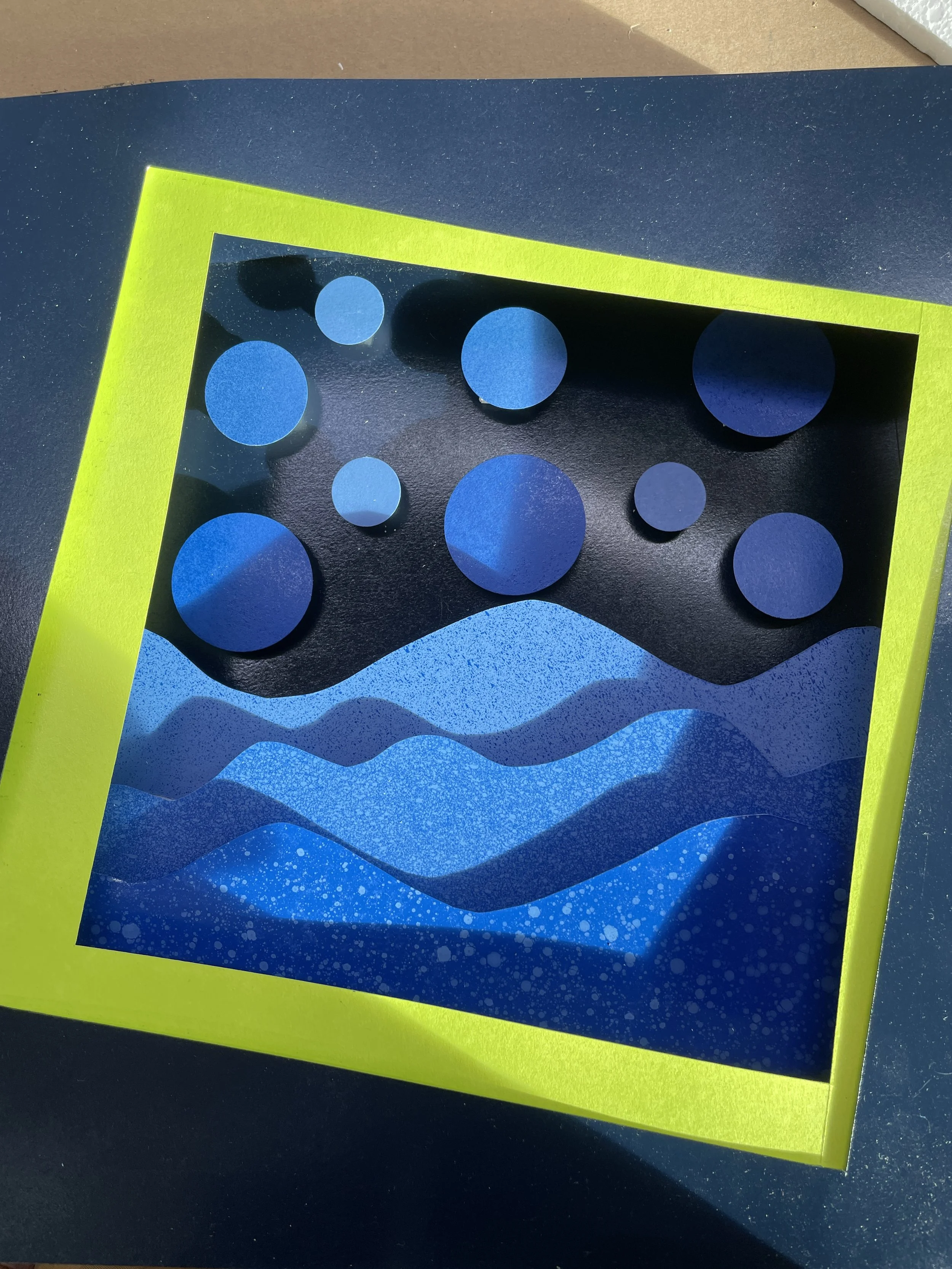 A close-up of a decorative piece with a yellow border, black background, and cutouts of blue circles and wavy patterns.