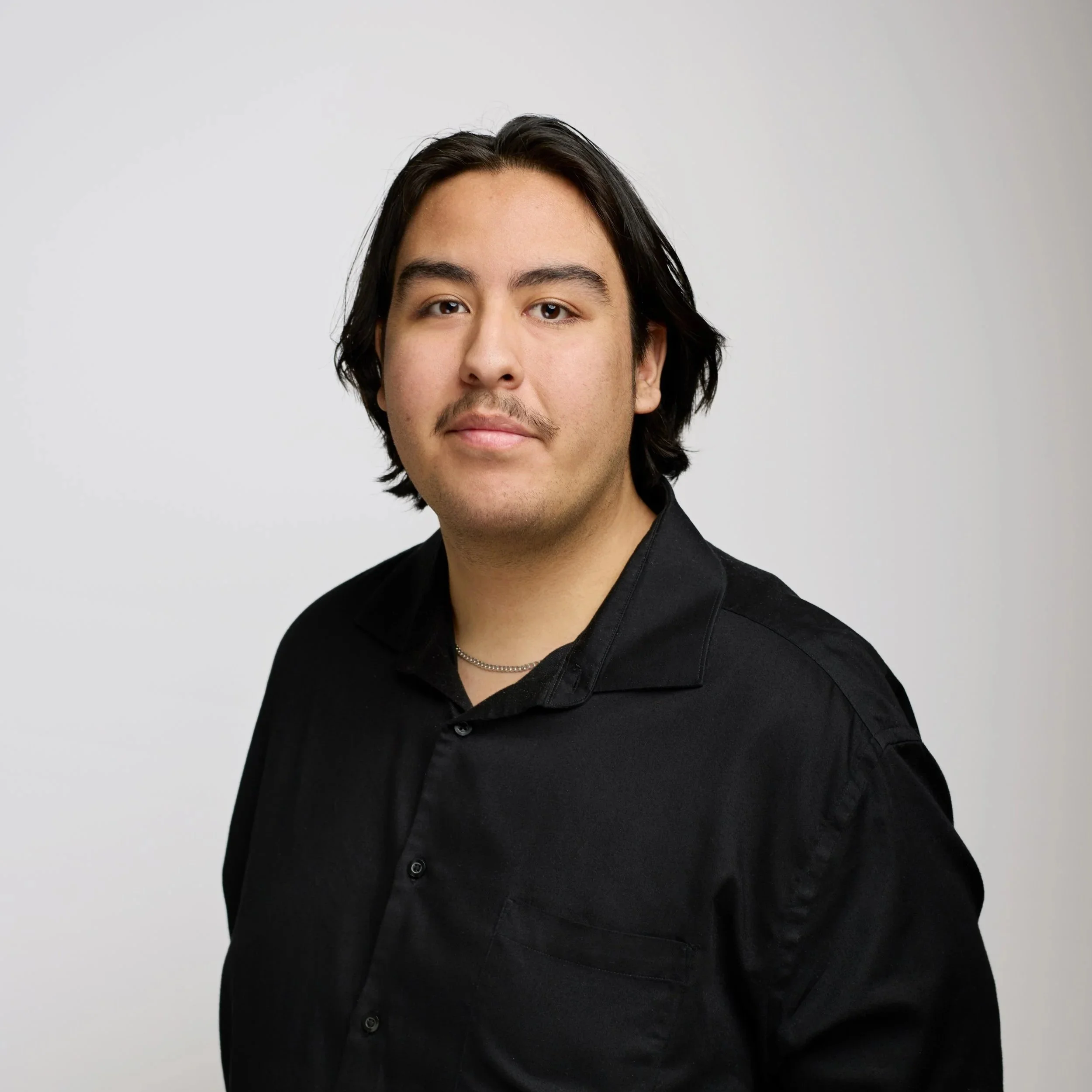 A woman with long blonde hair wearing a black top, smiling, against a black background.