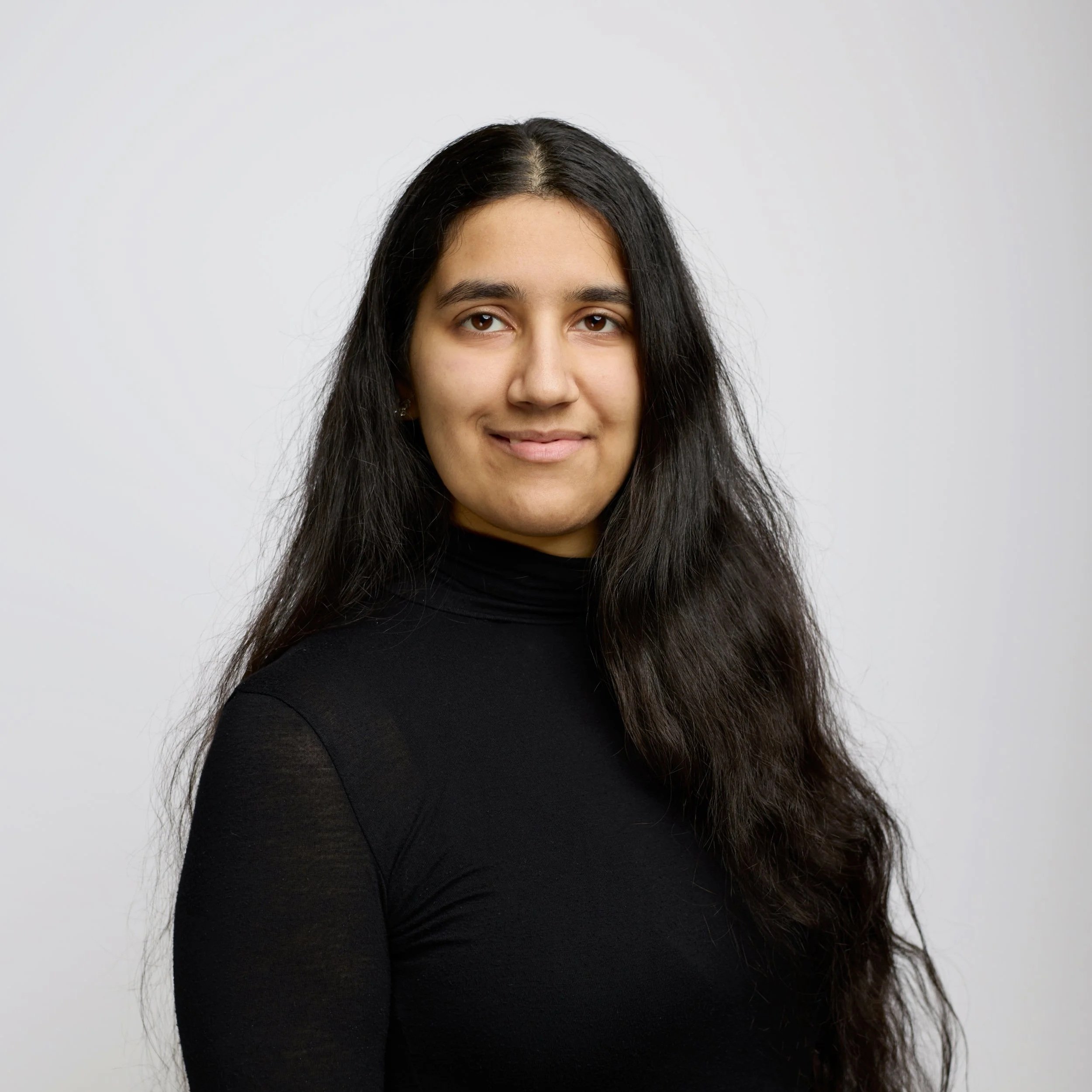 Portrait of a young woman with long, wavy brown hair, smiling, against a black background.