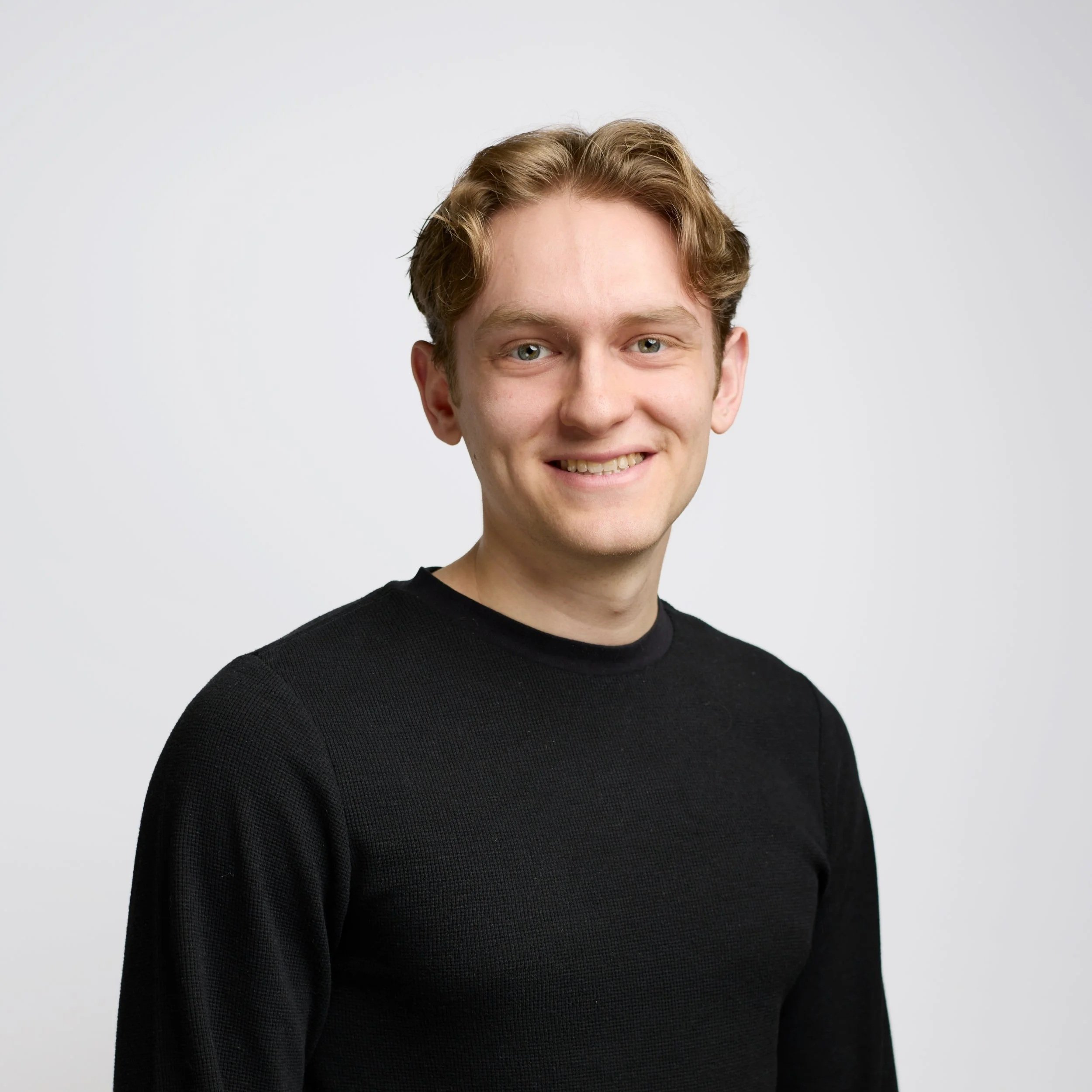 A portrait of a young woman with long black hair, wearing a black blazer and a cross necklace, against a black background.