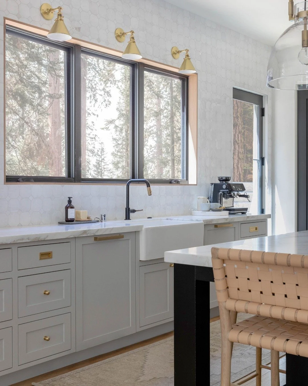 The kitchen at our #GroundedWarmth project is all about the mix of materials. Soft gray cabinetry is grounded by the darker island, while oak, brass accents, and marble bring contrast throughout. We carried the tile all the way up the wall to give th
