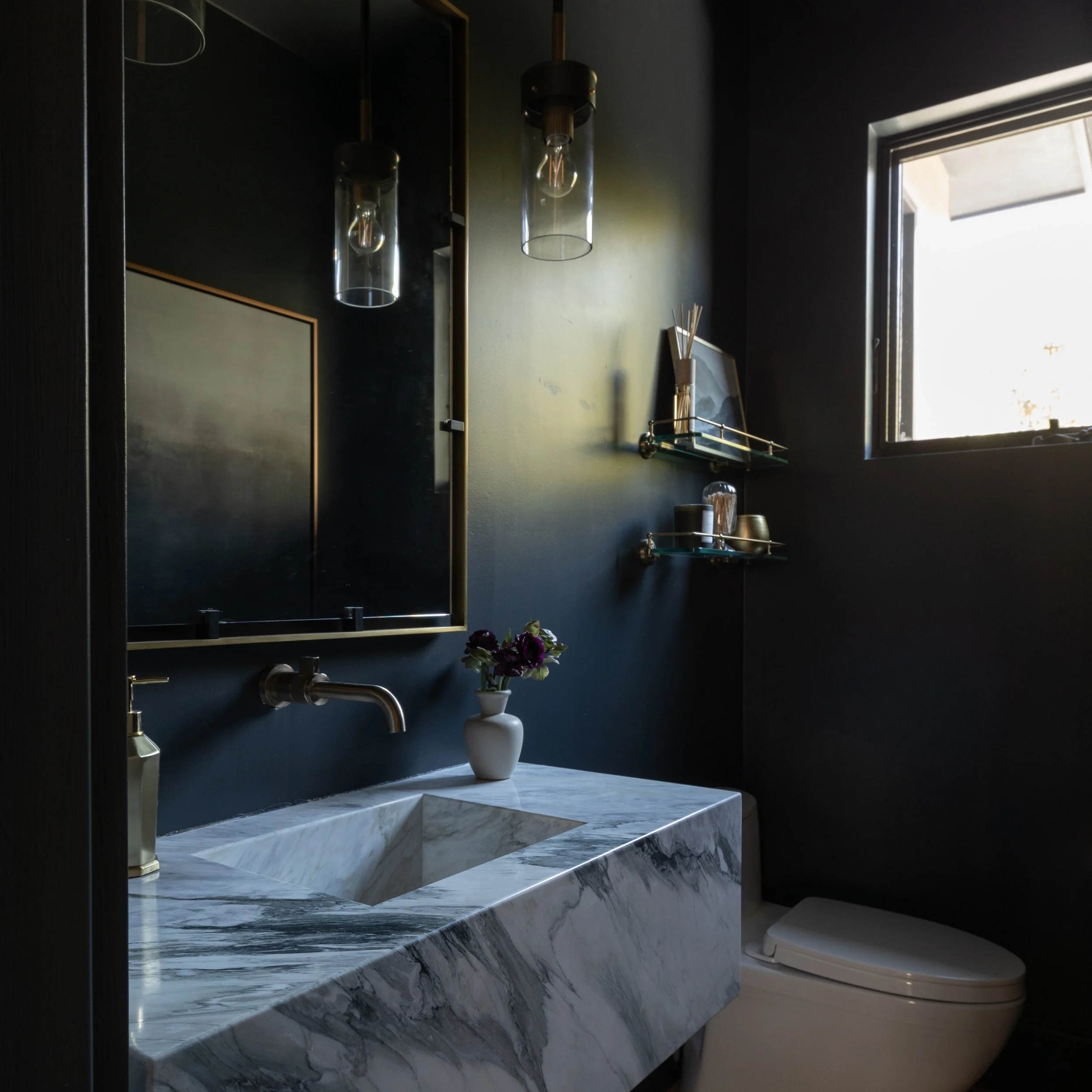 Moody powder room with dark walls, marble vanity, brass details and pendant lighting