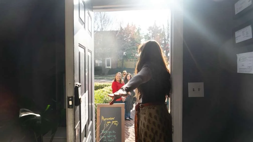 Holistic Hair Studio owner Leah Lattus greeting clients at the door in Alexandria VA,  warm sunlight welcomes three smiling women for organic hair services