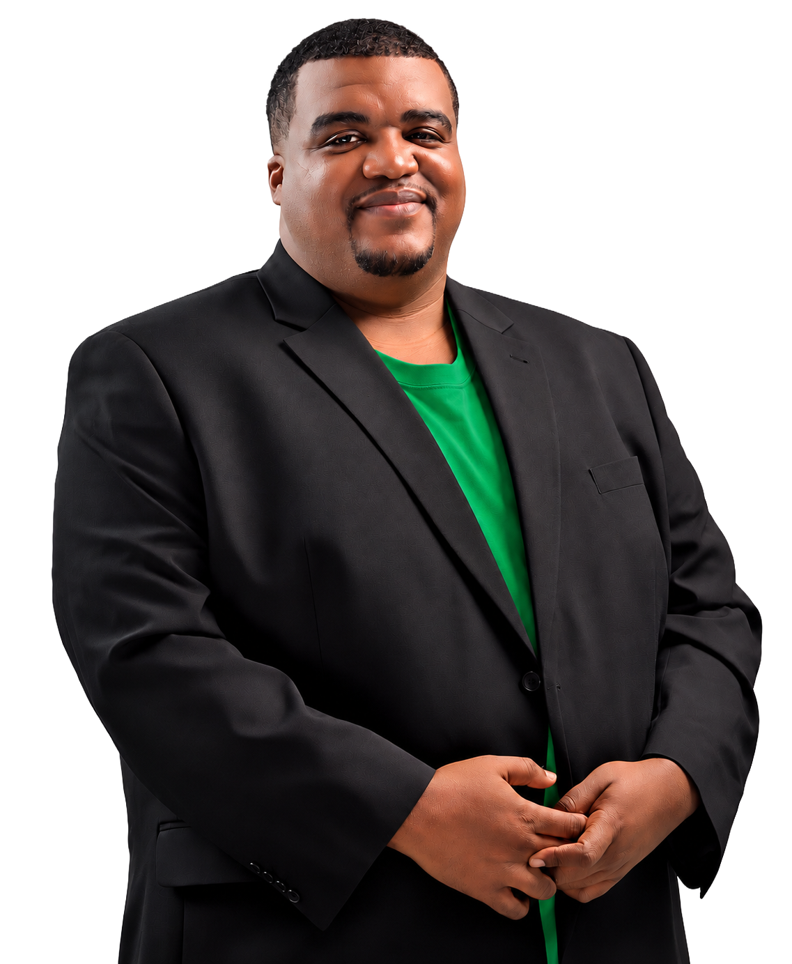 A man in a black blazer and green shirt, standing with hands clasped, smiling at the camera.