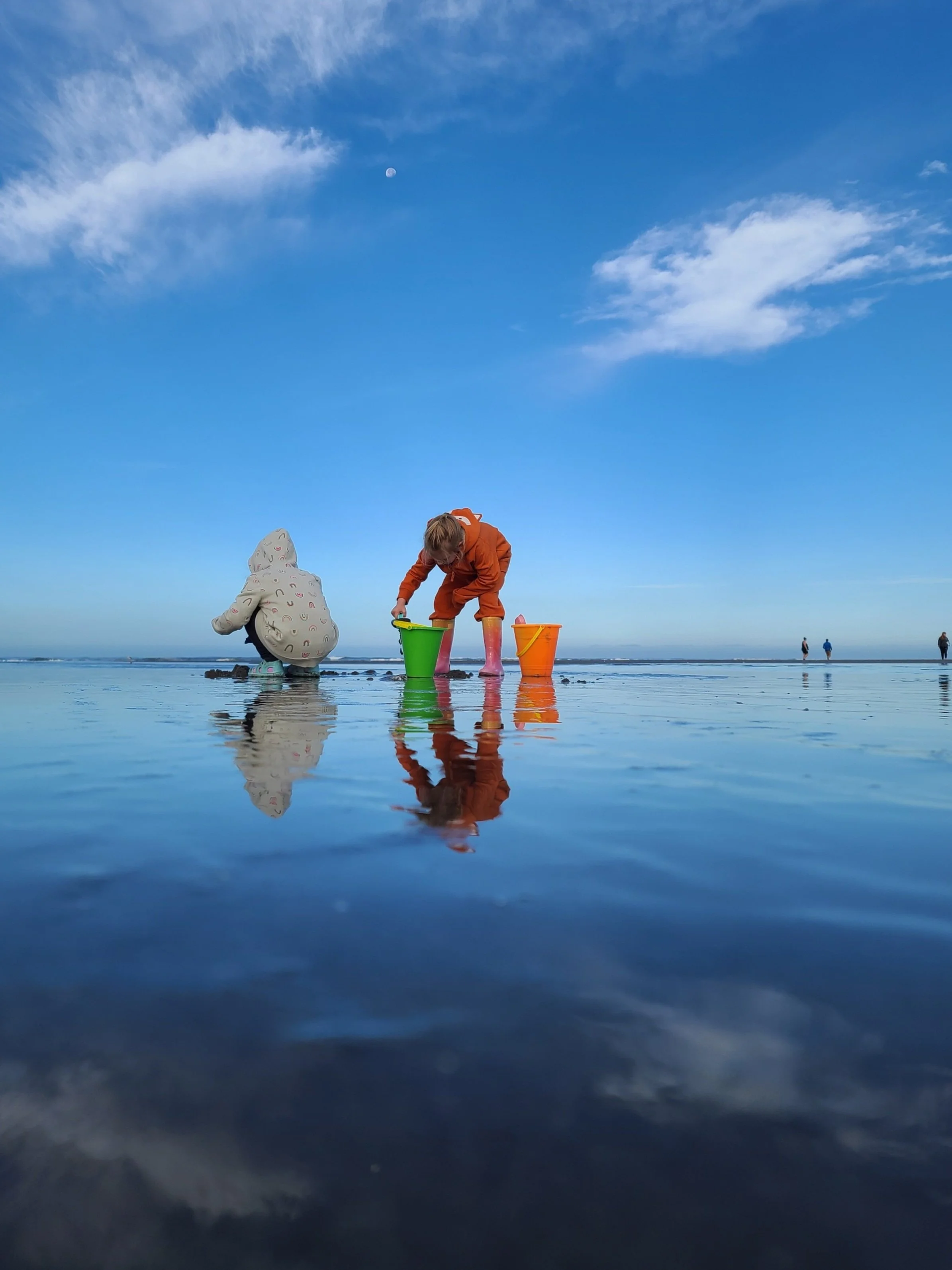 2 children play with sand on Seaside Oregon beach, with Moon peaking through sky