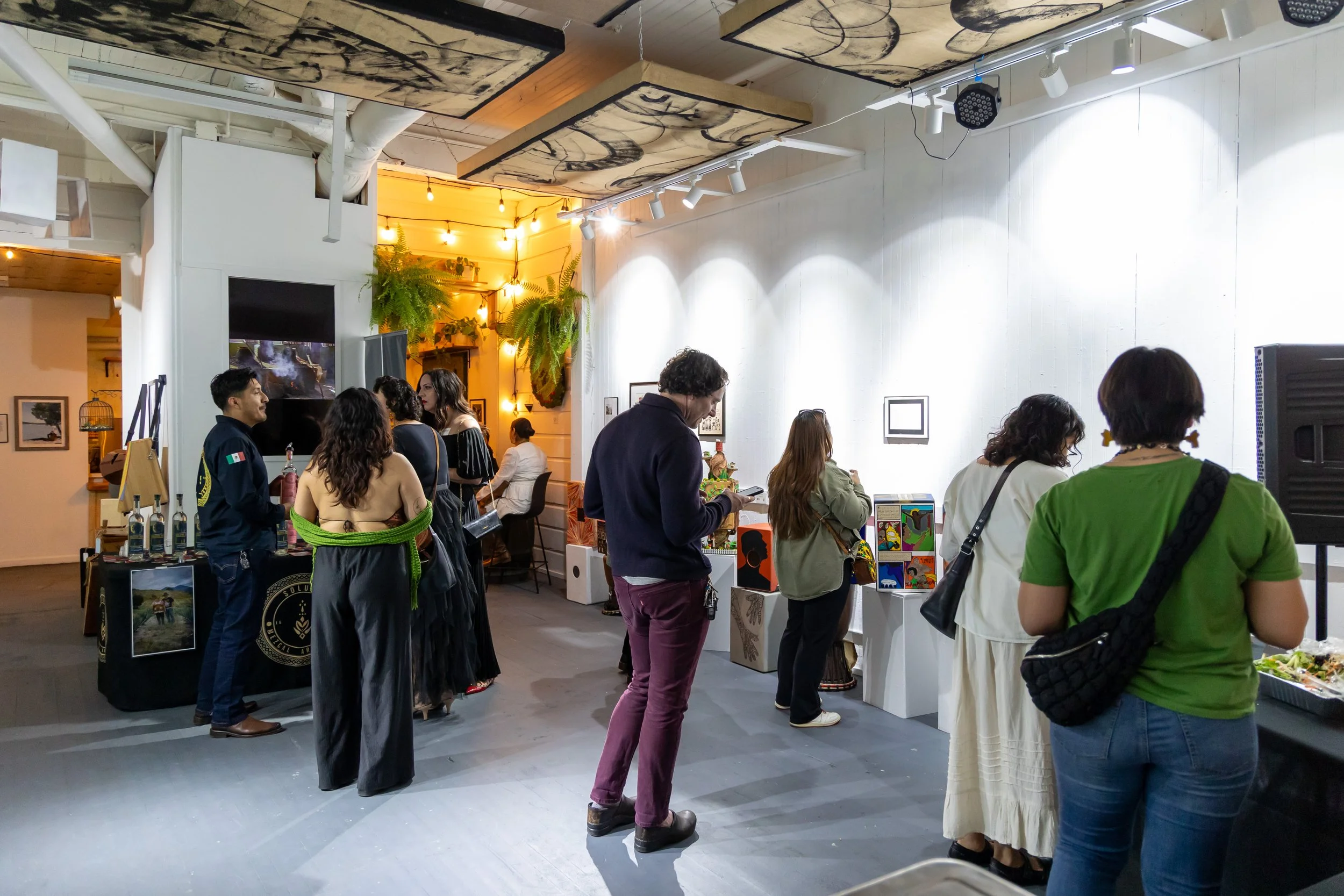 Gala-guetza guests mingling in mezcal vendor and food room. 