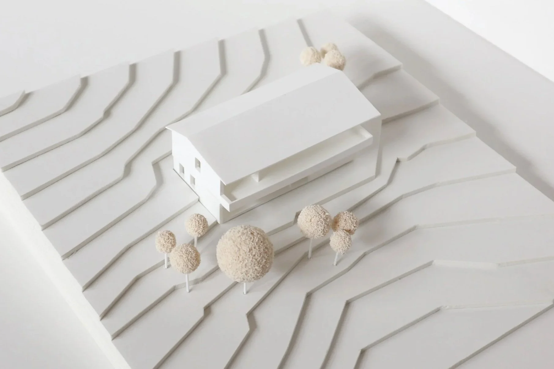 Architektonisches Modell eines weißen Hauses auf einem landschaftlichen Gelände 