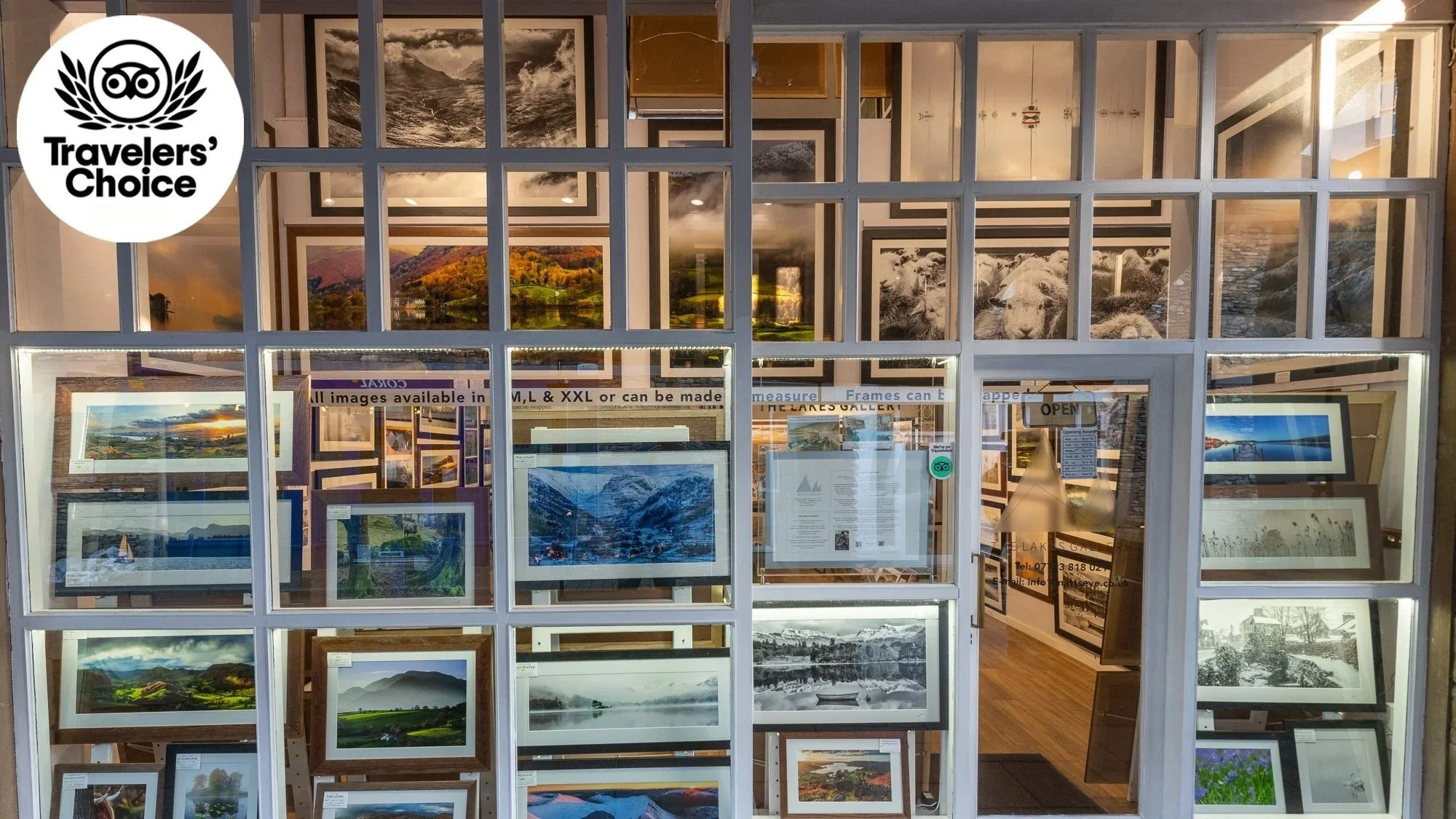 View of an art gallery with landscape photographs displayed inside, seen through a front window with a grid pattern. The gallery has a 