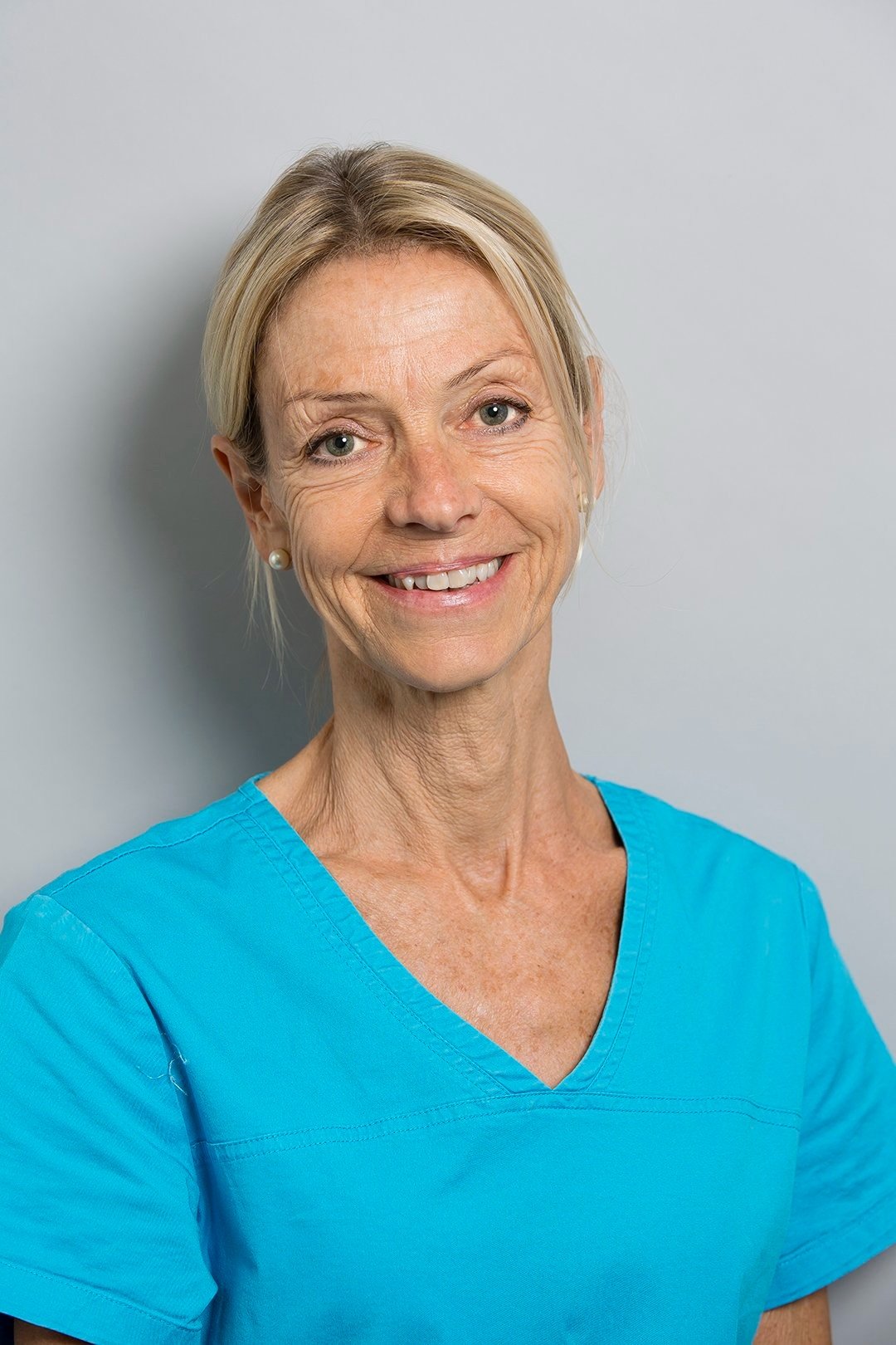 Femme souriante en tenue médicale bleue.