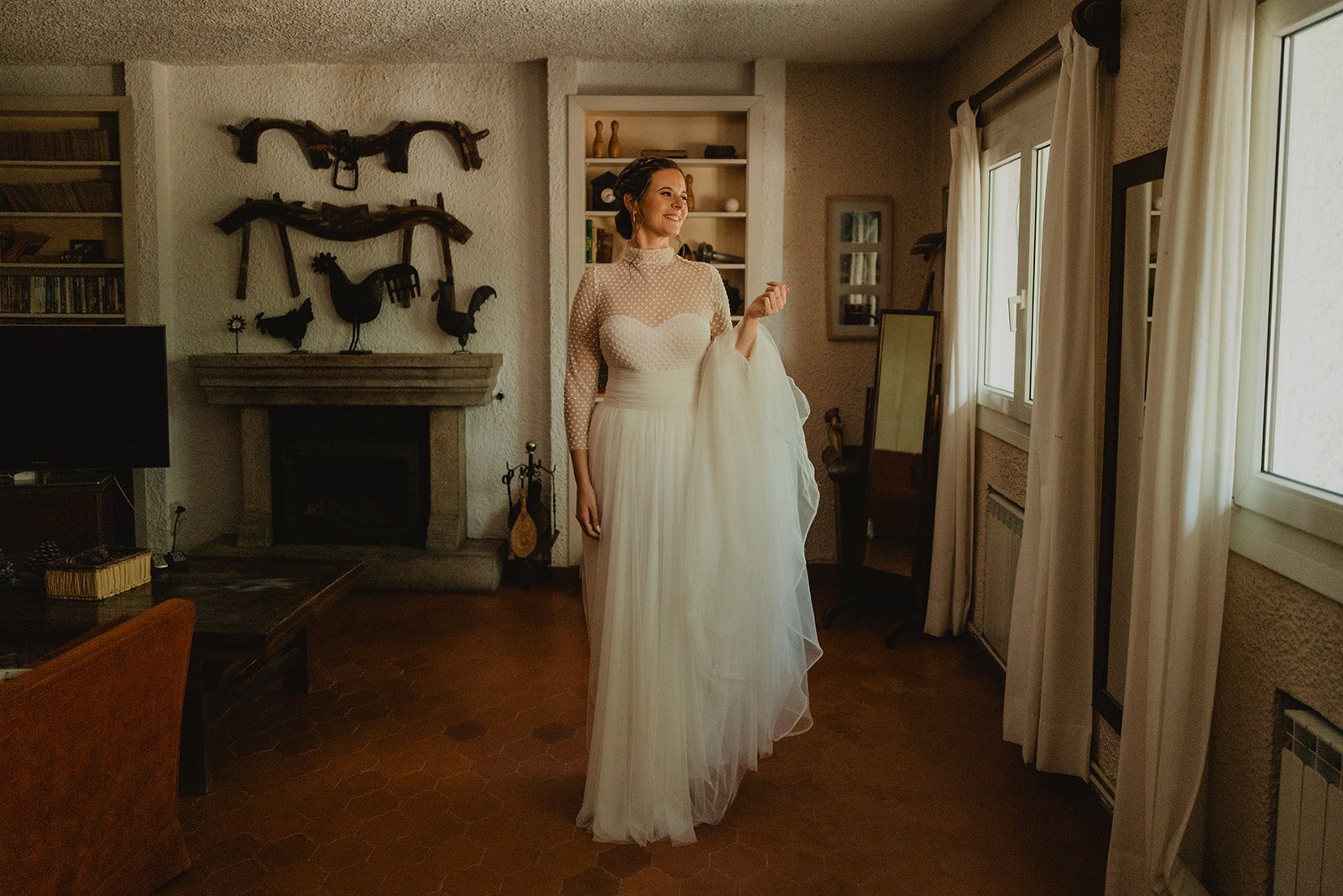 Novia con vestido blanco en una sala rústica con chimenea de fondo.