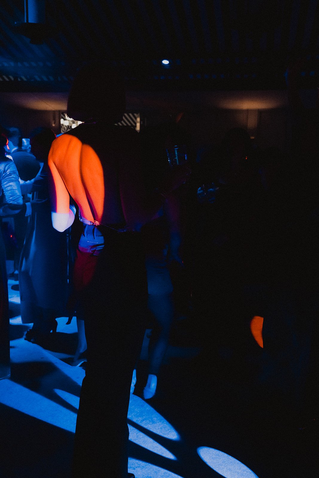 Personas bailando en un club nocturno iluminado por luces de colores, predominando tonos azules y rojos.