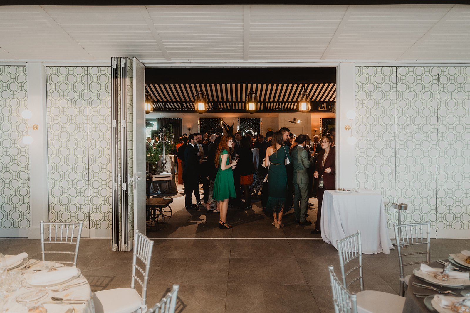Recepción en un evento con varias personas socializando en un salón decorado con mesas y sillas elegantes.