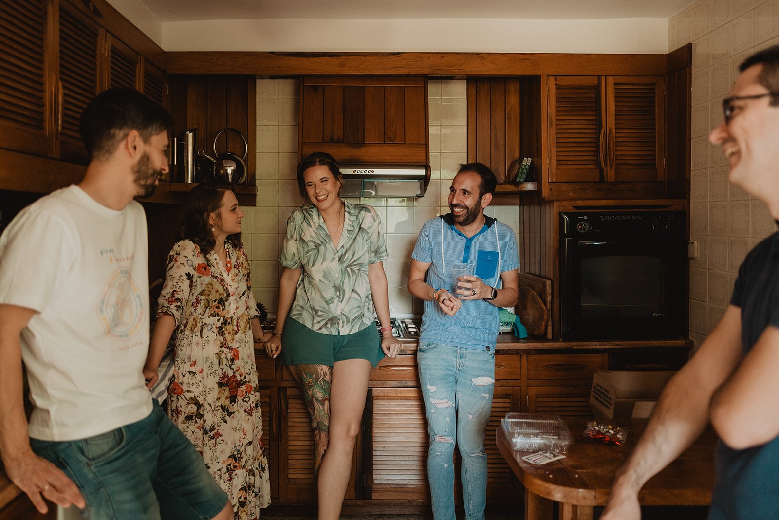 Un grupo de personas conversando y riendo en una cocina con muebles de madera.