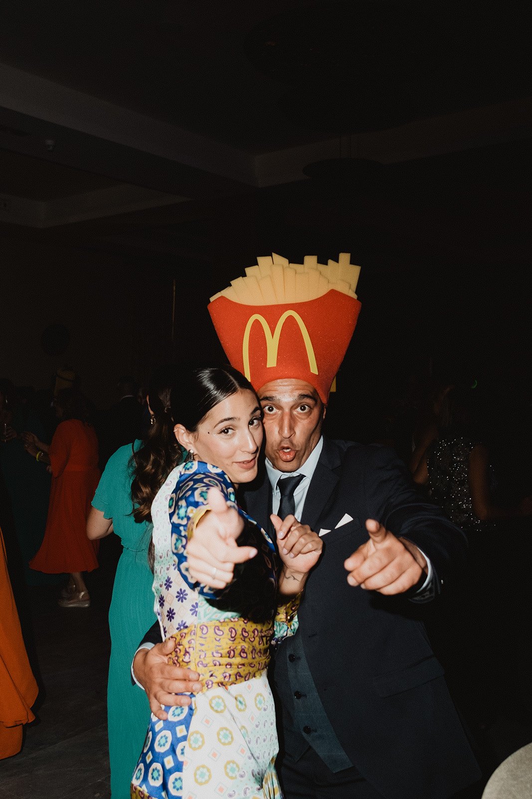 Dos personas posando, una con un disfraz de papas fritas de McDonald's en una fiesta.