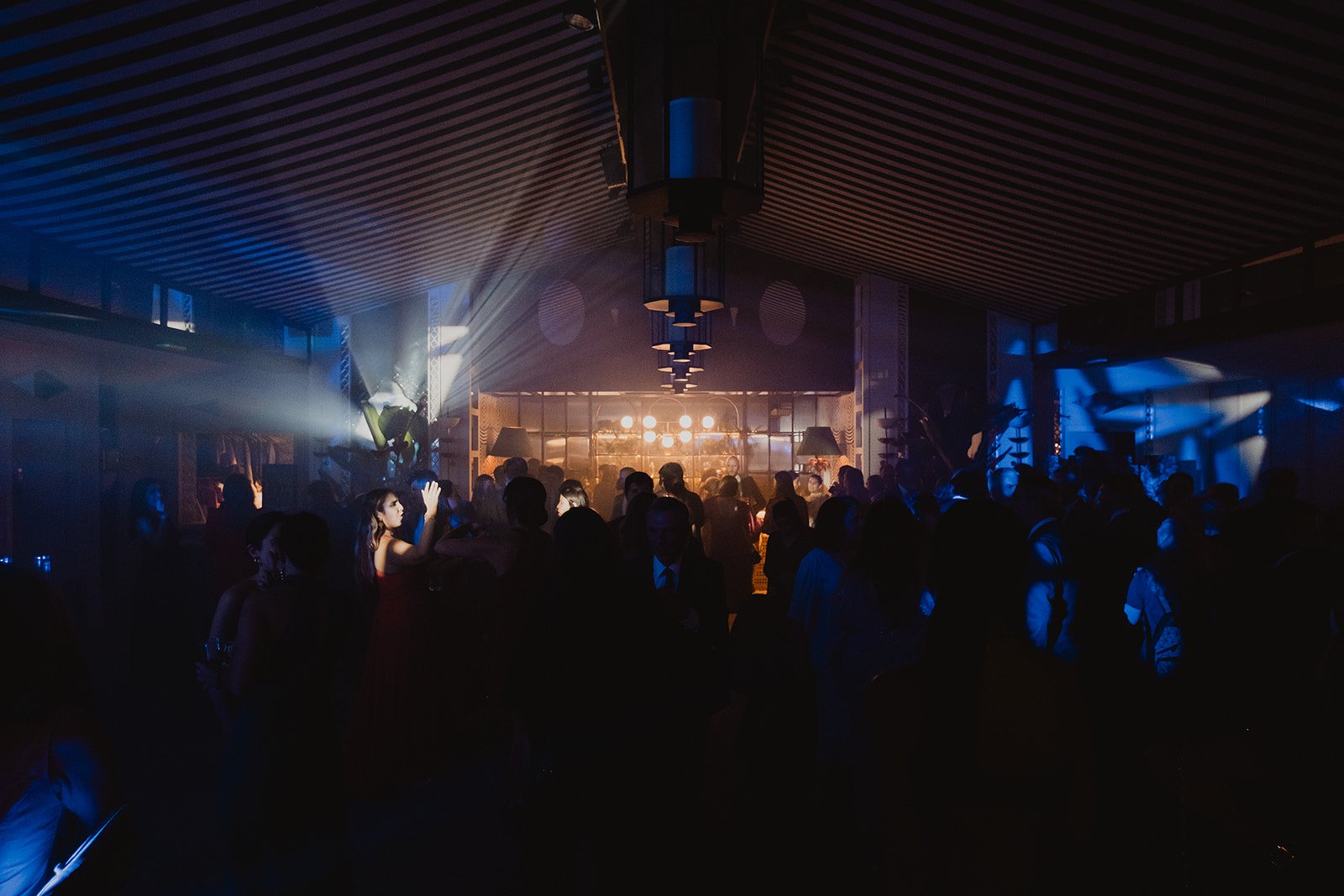 Personas bailando en una fiesta con luces de colores y música, ambiente oscuro.