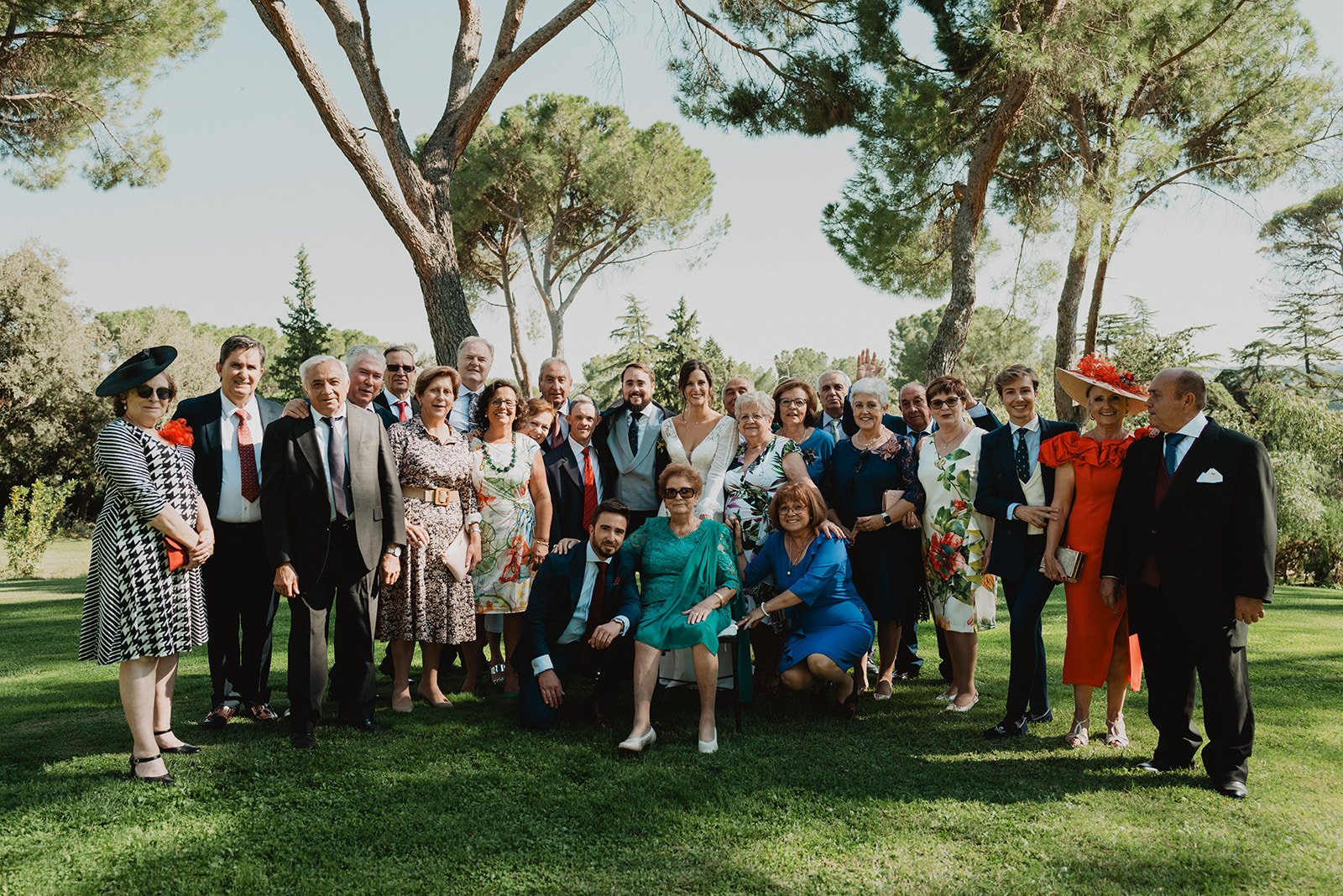Grupo de personas posando al aire libre, posiblemente en un evento formal o una boda, rodeados de árboles.