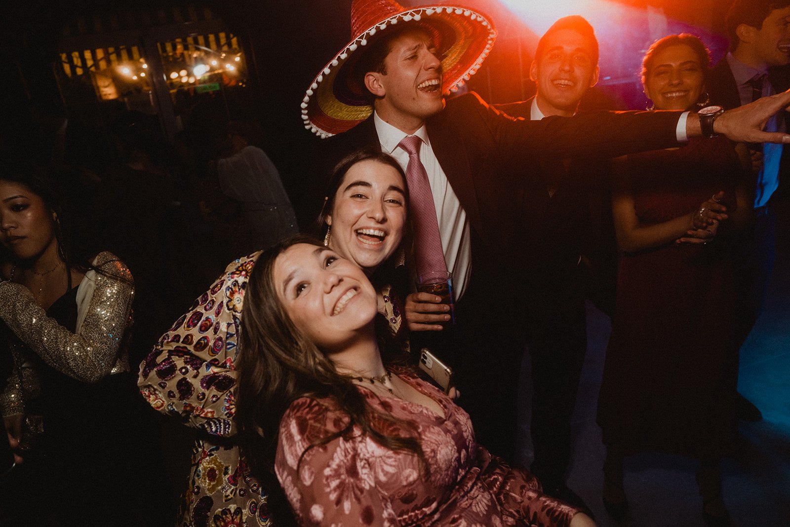 Grupo de personas sonriendo y posando en una fiesta, uno de ellos lleva un sombrero mexicano.