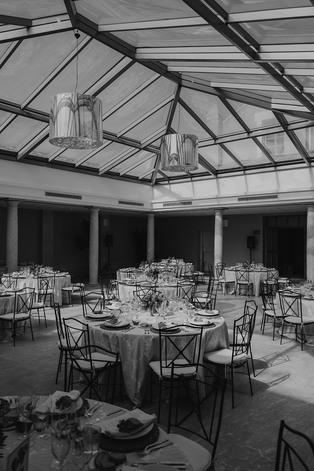 Salón de eventos con mesas redondas, sillas de metal y techo de vidrio.