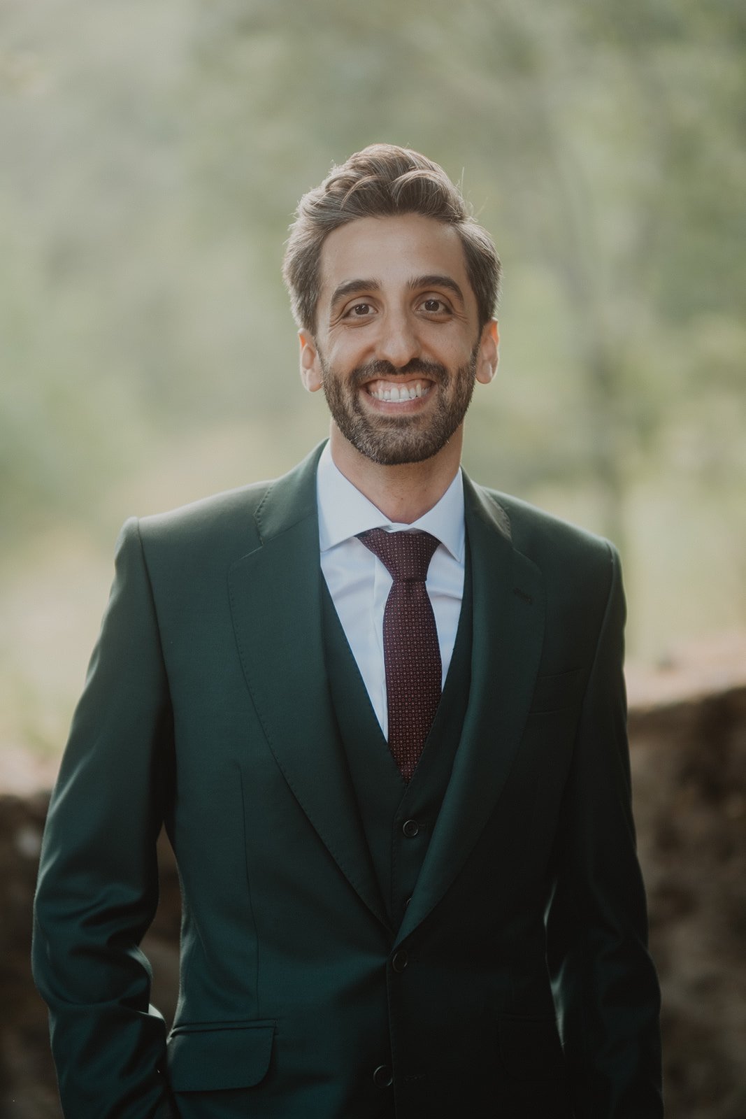 Hombre sonriendo con traje formal oscuro al aire libre.