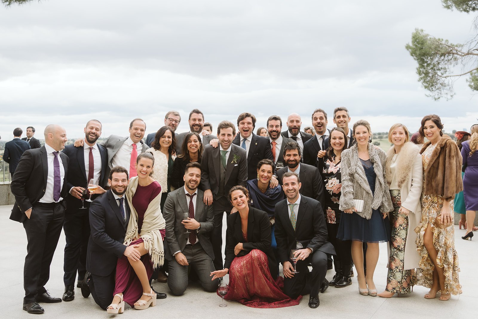 Grupo de personas vestidas elegantemente sonriendo en un evento al aire libre.