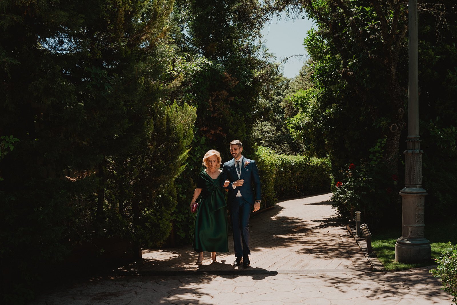 Dos personas caminando en un parque rodeadas de vegetación.