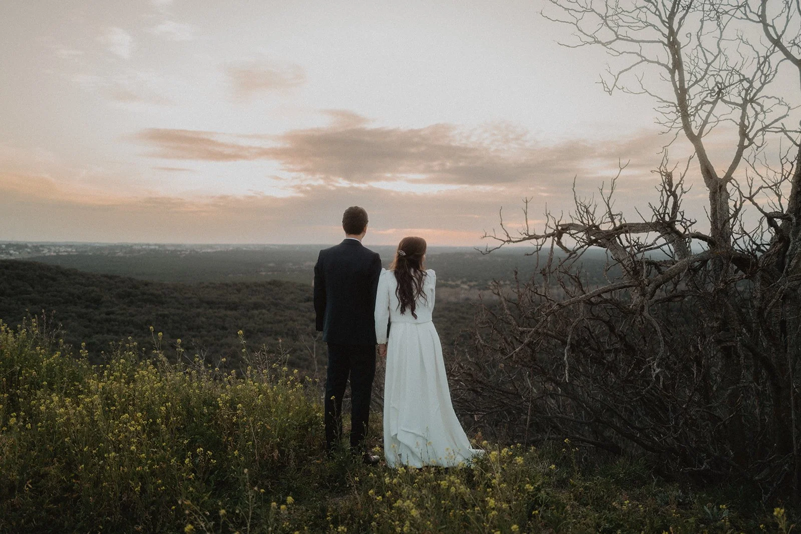 Pareja de espaldas en un campo mirando al horizonte durante el atardecer.