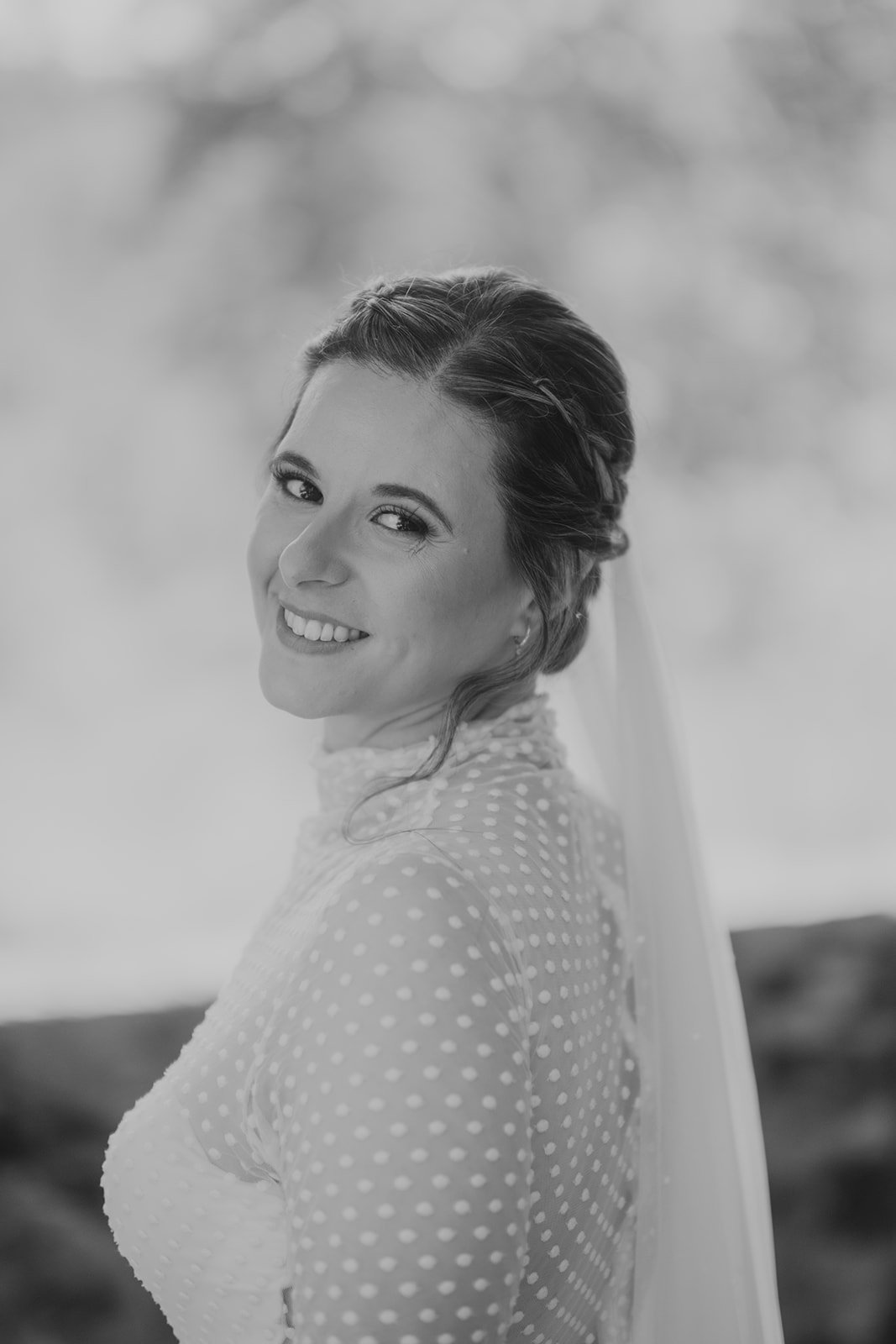 Retrato en blanco y negro de una mujer con vestido de lunares y velo, sonriendo y mirando hacia atrás.