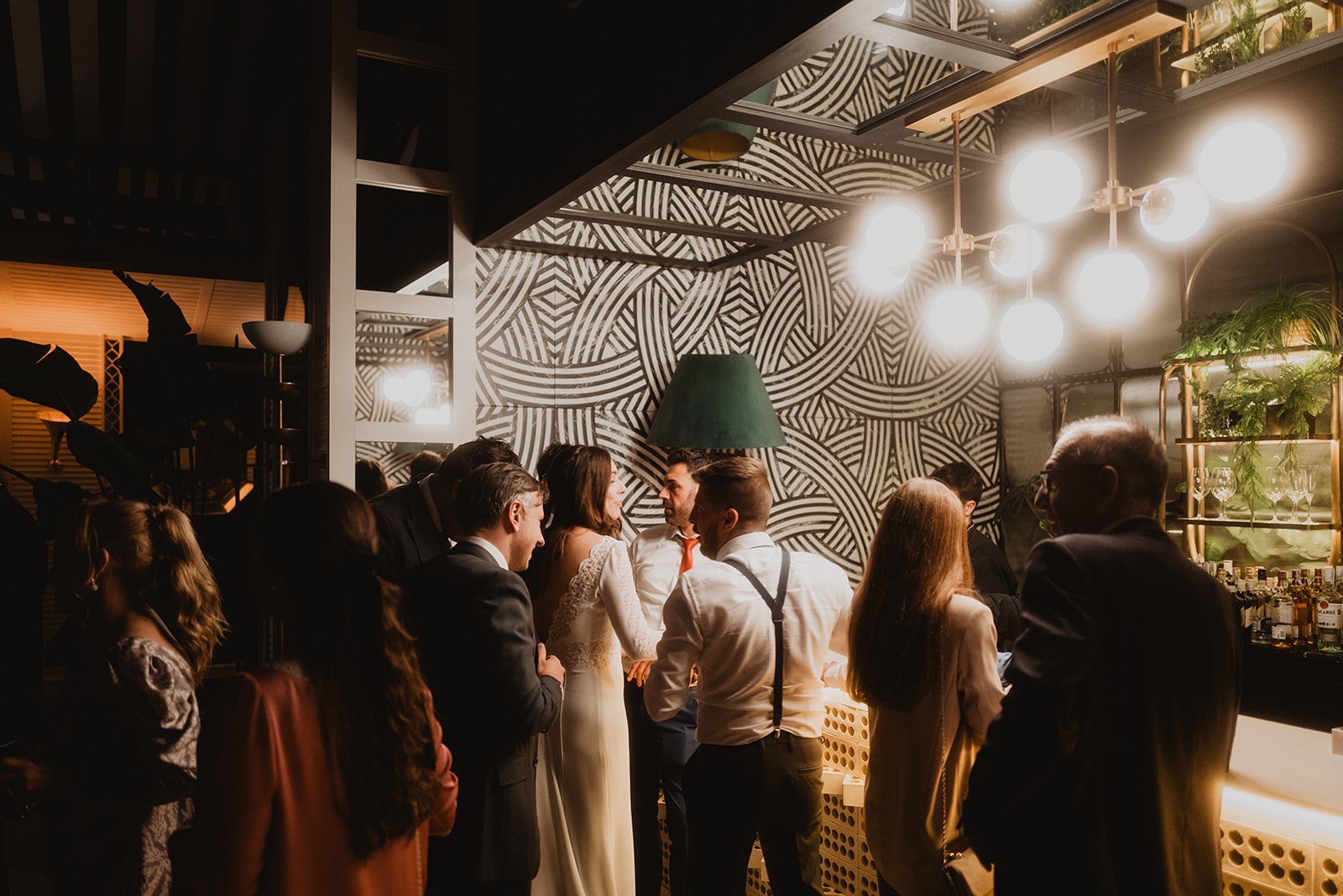 Grupo de personas en una fiesta, conversando en un bar interior con luces brillantes y decoración moderna.
