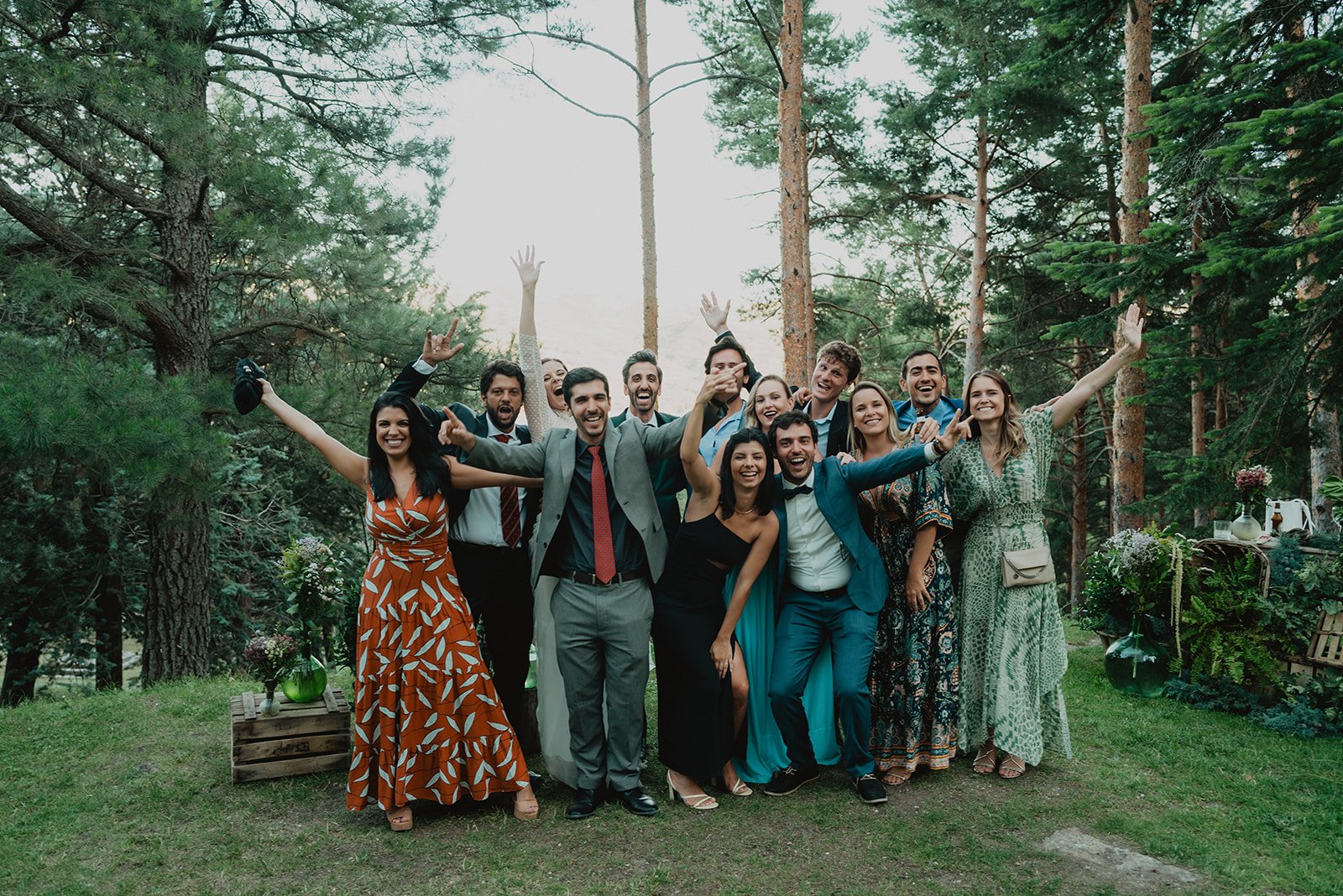 Grupo de personas sonrientes posando al aire libre, rodeados de árboles y plantas, vestidos de forma elegante.