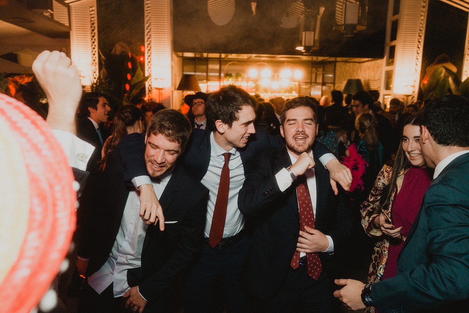Grupo de personas jóvenes sonriendo y divirtiéndose en una fiesta o evento social, vistiendo trajes formales.