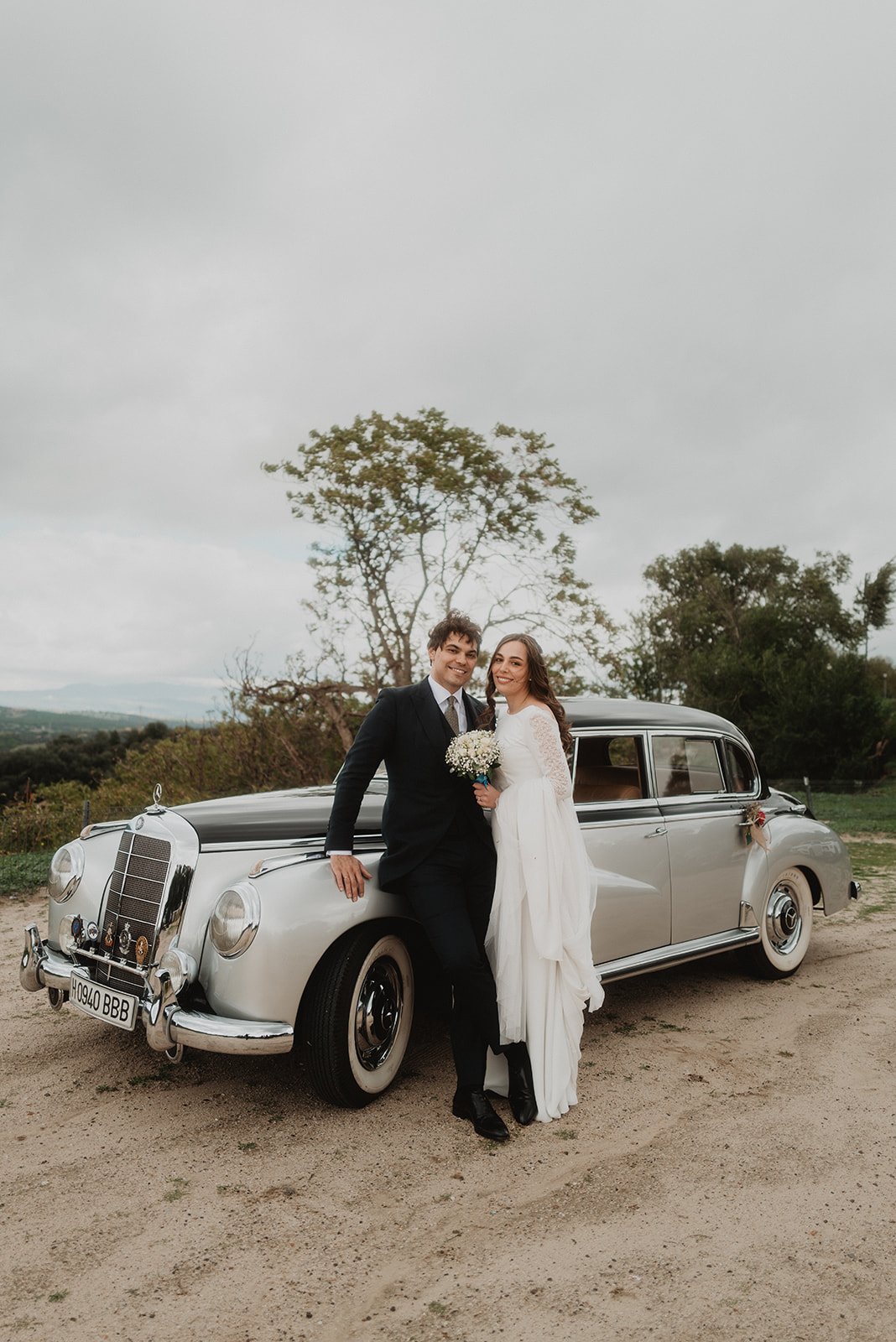 Pareja de recién casados junto a un automóvil clásico en un entorno al aire libre.