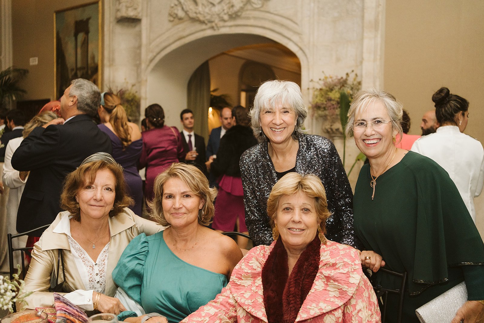 Grupo de mujeres sonrientes en un evento formal con otras personas en el fondo.