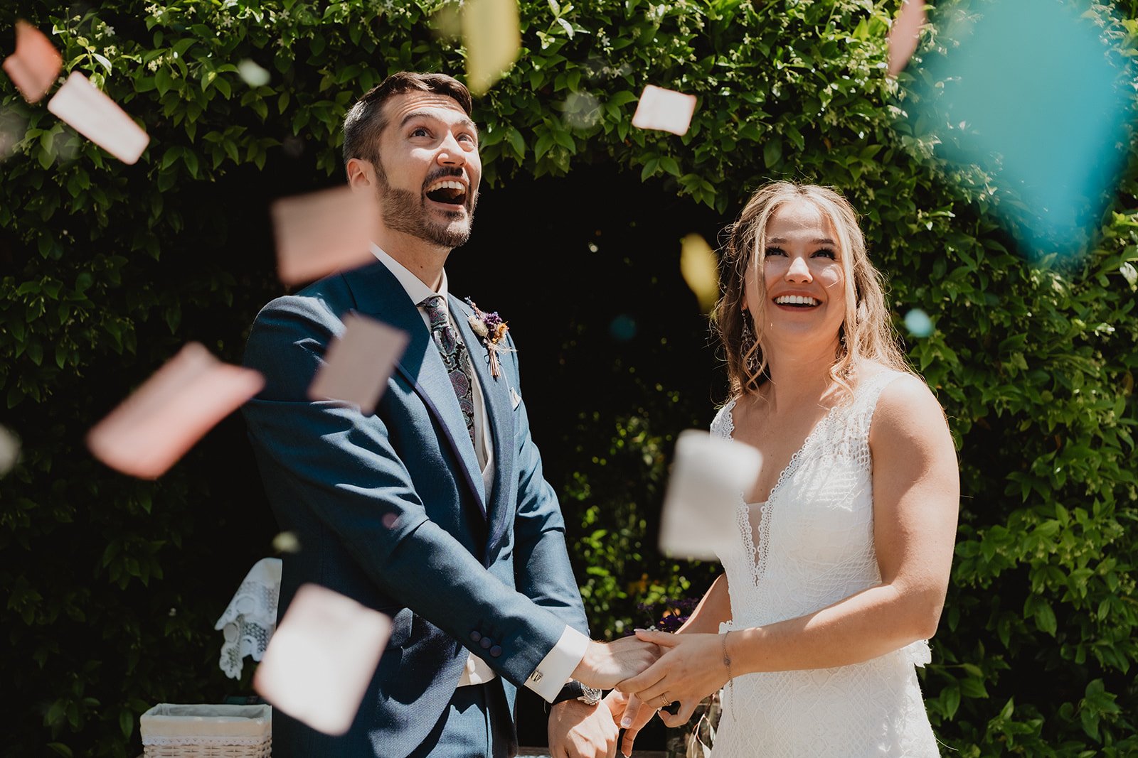 Pareja de recién casados sonriendo mientras caen pétalos de colores alrededor.