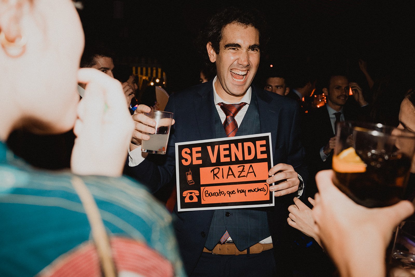 Hombre sonriendo en una fiesta, sosteniendo un letrero que dice "Se vende Riaza".