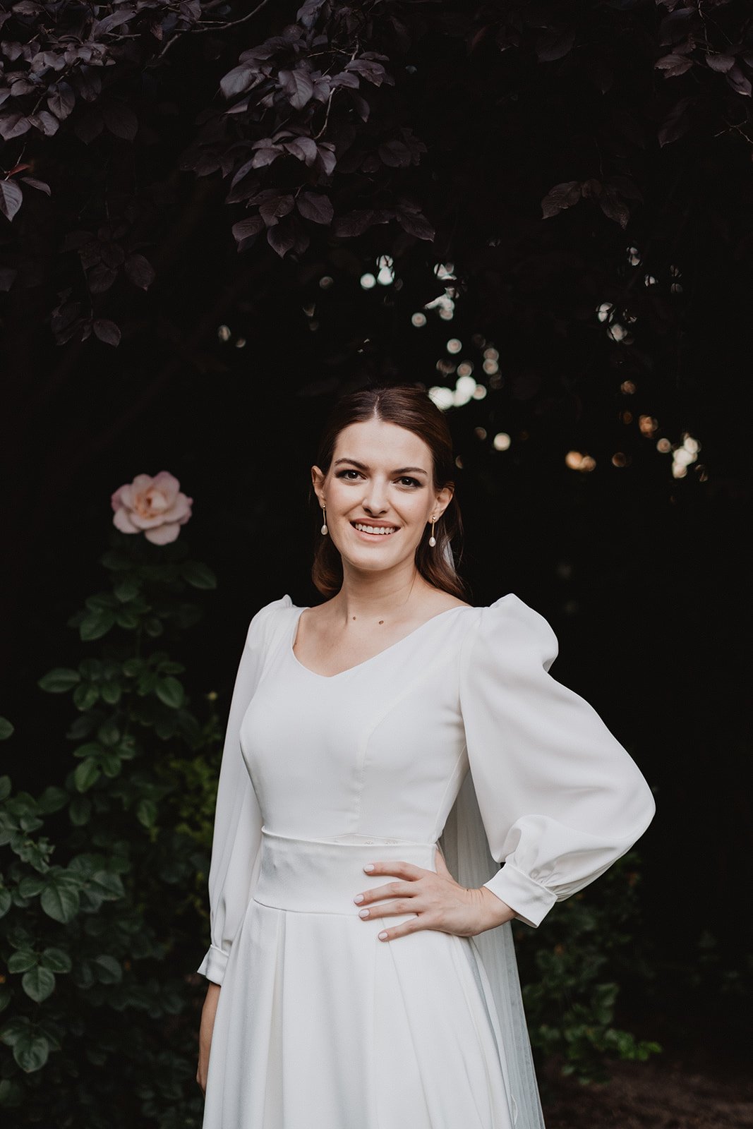 Mujer con vestido blanco, fondo de jardín oscuro con flores.