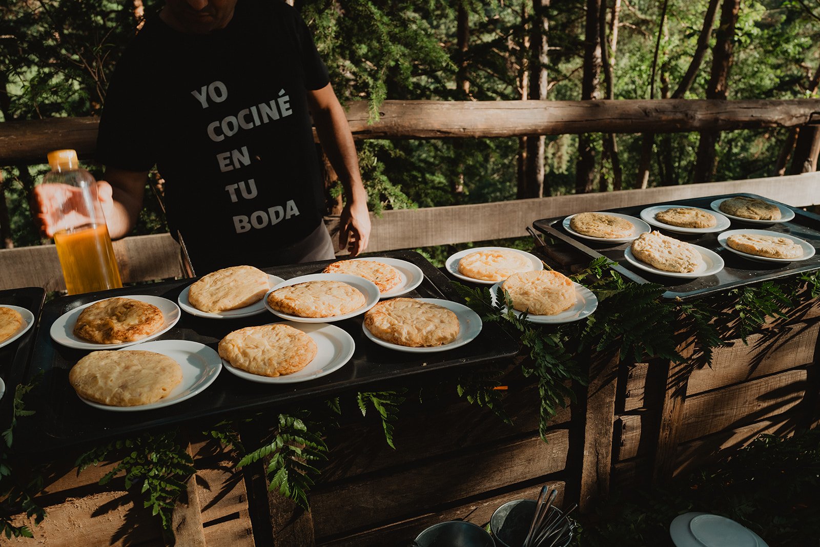 Persona sirviendo tortillas en platos situados sobre una mesa al aire libre, rodeada de vegetación.