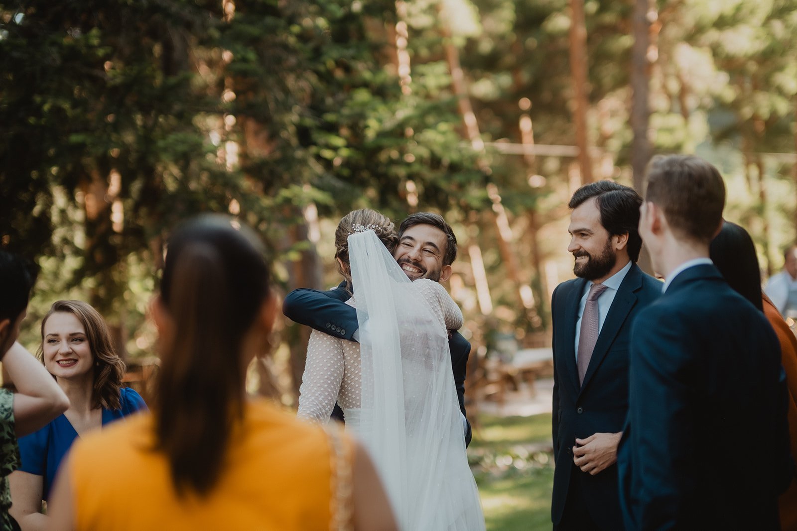 Personas celebrando en un evento al aire libre, posiblemente una boda, con árboles de fondo.