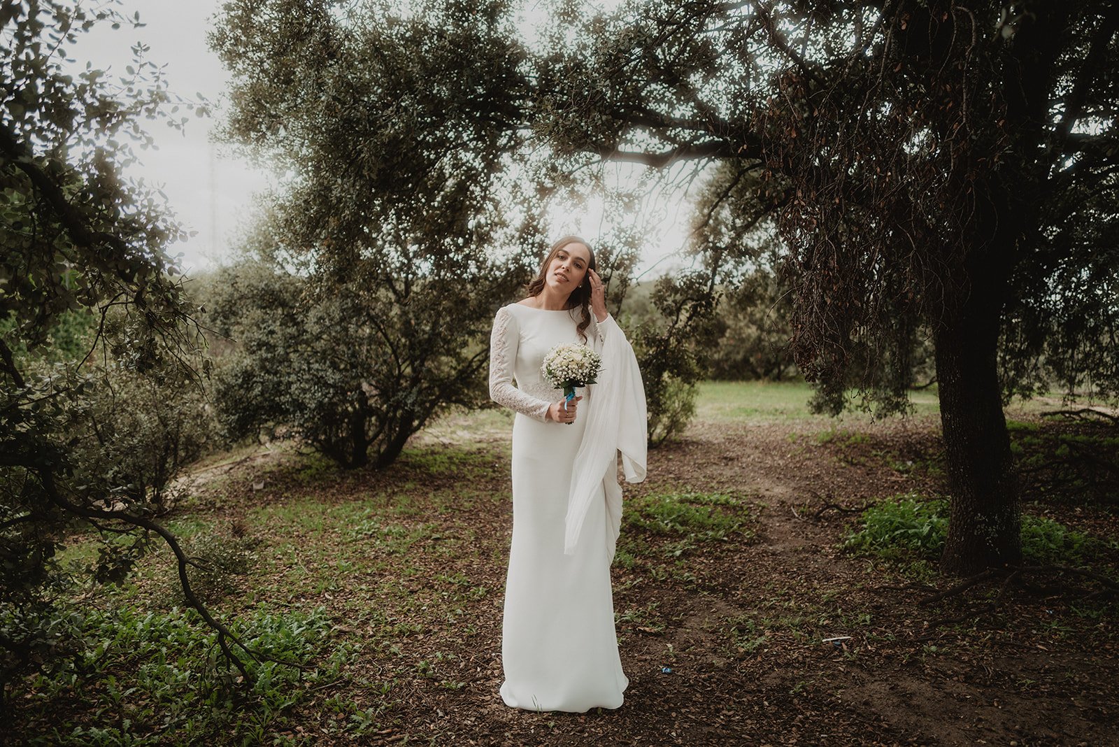 Novia con vestido blanco y ramo en un bosque.