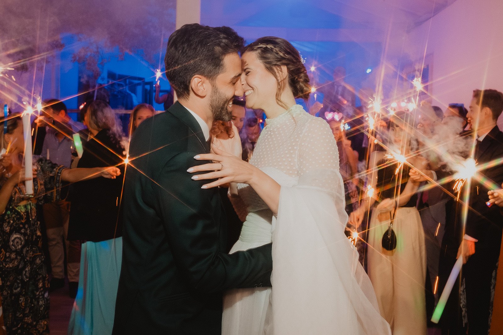 Pareja abrazándose en una fiesta con bengalas alrededor.