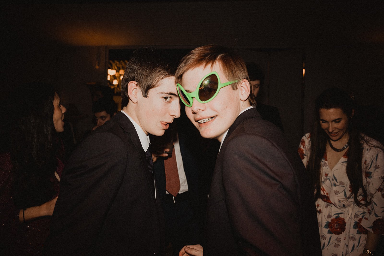 Grupo de jóvenes en una fiesta, uno con gafas verdes grandes, sonriendo y divirtiéndose.