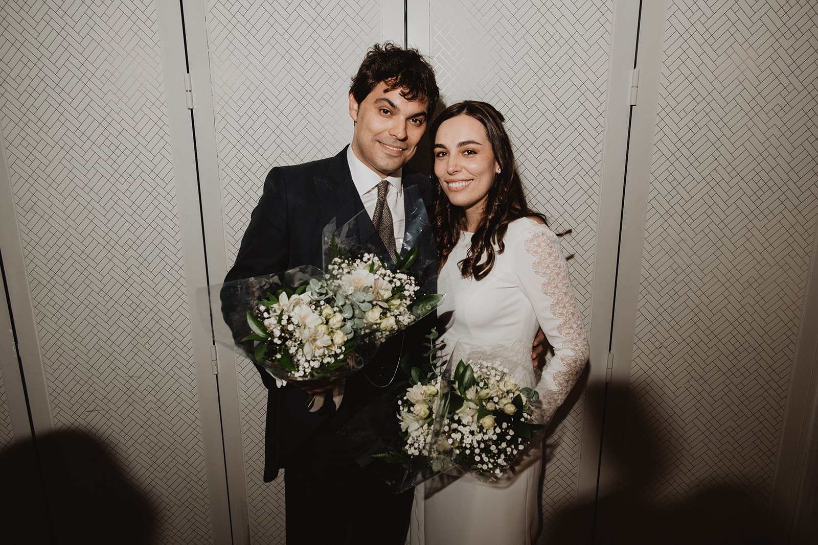 Pareja sonriente en traje formal con ramos de flores.