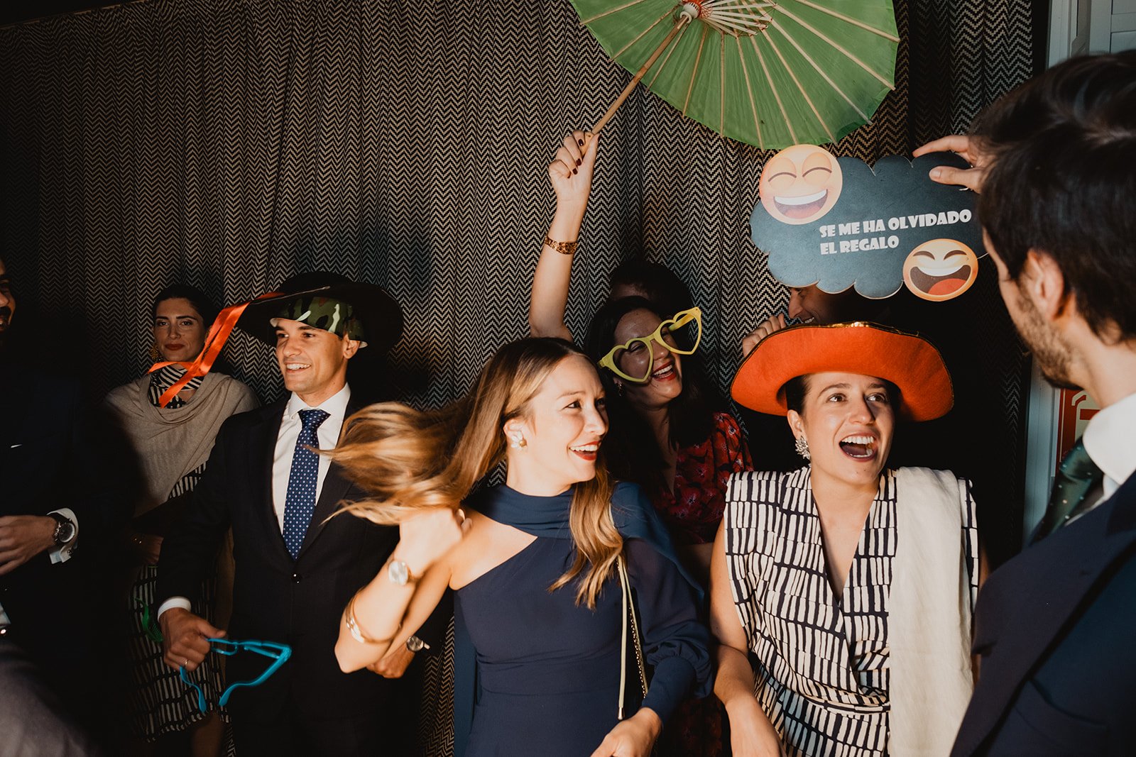 Personas riendo y usando disfraces divertidos en una fiesta con fondo de cortina estampada.