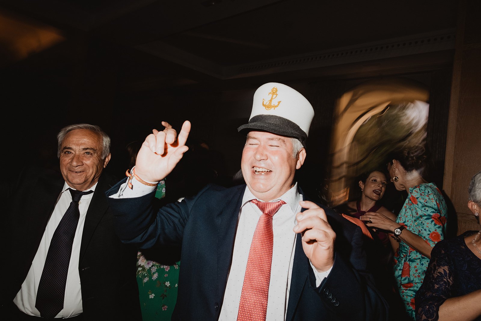 Hombre sonriente con sombrero de capitán, rodeado de personas en una fiesta.