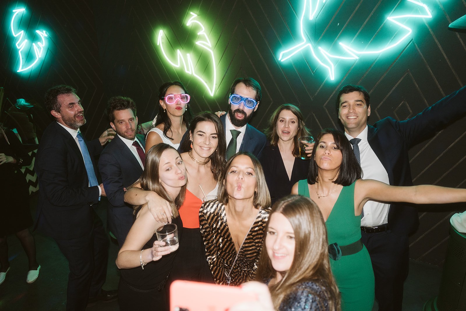 Grupo de personas en una fiesta, sonriendo y posando para una foto, con luces de neón verde en el fondo.