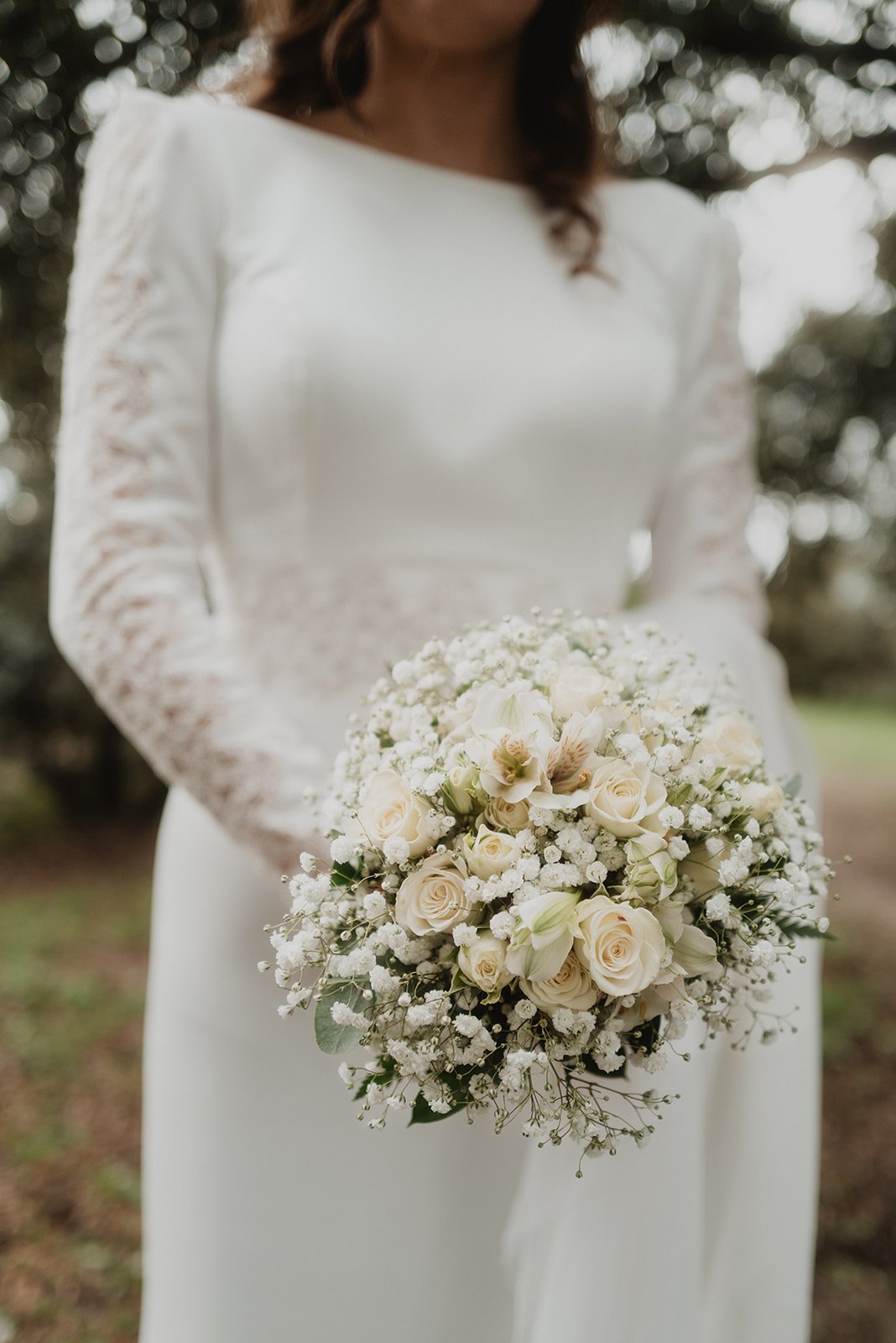 Novia con vestido blanco sosteniendo un ramo de flores blancas y crema.
