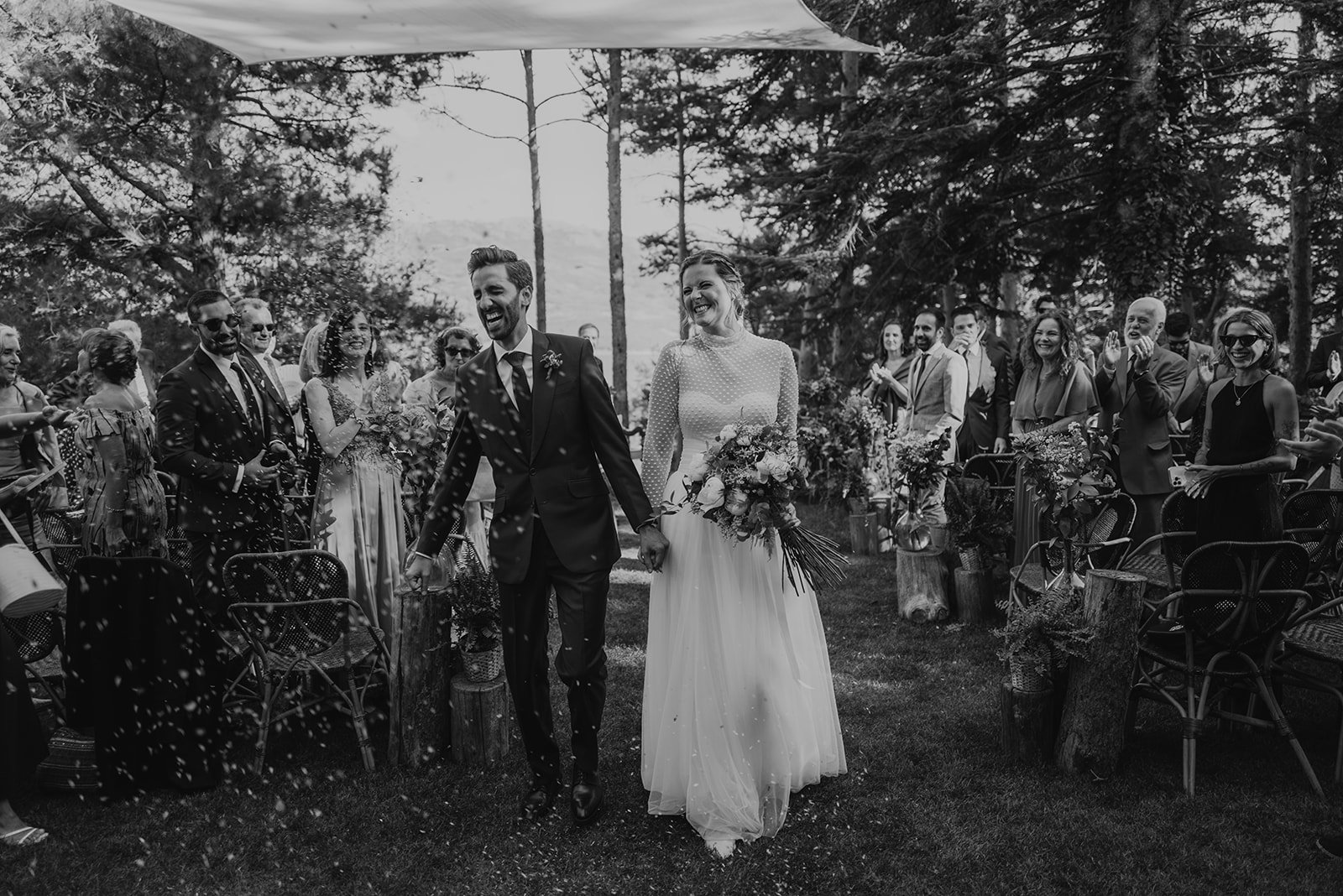 Pareja de recién casados caminando por el pasillo al aire libre mientras los invitados celebran.