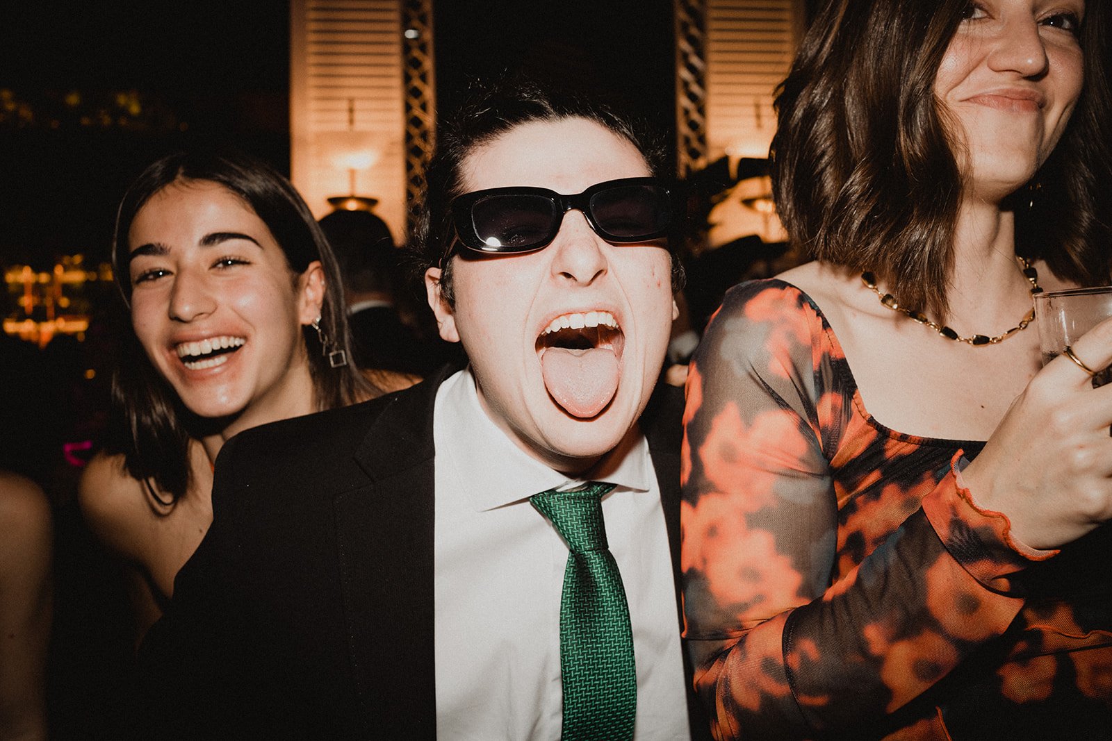 Grupo de personas jóvenes divirtiéndose en una fiesta, una de ellas mostrando la lengua y usando gafas de sol.