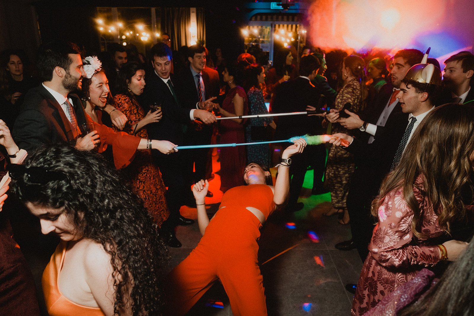 Personas divirtiéndose en una fiesta; alguien haciendo el juego del limbo con luces y música.