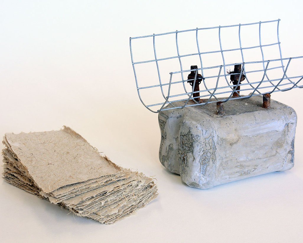 Cast concrete pint milk carton, found farm machinery parts, straw paper.