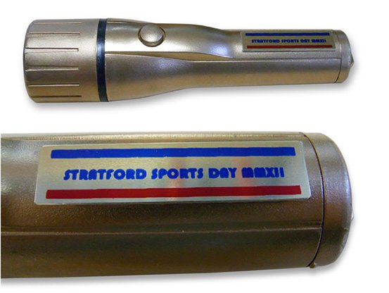 Gold flashlight with a button on its side and a label reading "Stratford Sports Day Maxii."